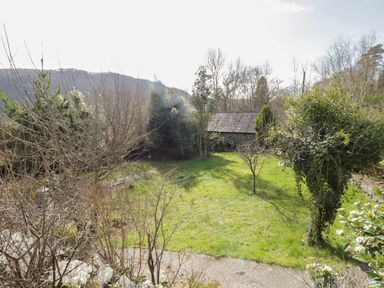 A garden with grass trees and a stone shed in the background at The Old Smithy Cottage Maentwrog near Penrhyndeudraeth