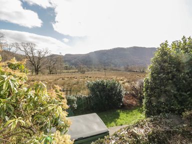 A garden with bushes and grass overlooking a field and hills at The Old Smithy Cottage Maentwrog near Penrhyndeudraeth