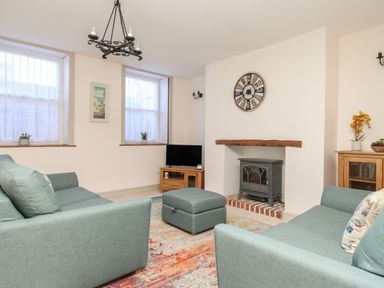 A living room with two teal sofas a gray stove in a fireplace a round clock on the wall a wooden cabinet and a colorful rug at Bliss On The Bay in Weymouth