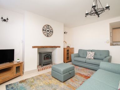 A living room with teal sofas a wooden TV stand a wall clock and a fireplace at Bliss On The Bay in Weymouth