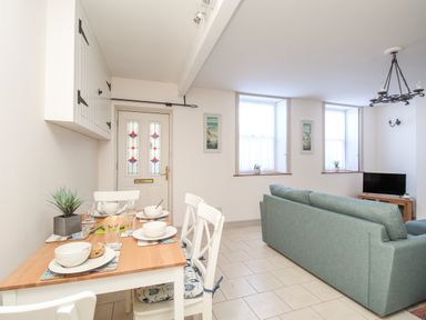 A dining area with four place settings and a seating area with a blue sofa and windows at Bliss On The Bay in Weymouth