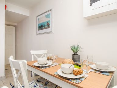 A dining area with a wooden table set for four people with white bowls plates and glasses and a small plant on the table at Bliss On The Bay in Weymouth