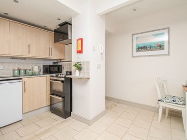 A kitchen with wooden cabinets a black oven microwave and a white chair with a cushion at Bliss On The Bay in Weymouth