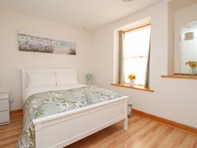 A bedroom with a white bed and floral bedcover a window with curtains and flowers in a vase at Bliss On The Bay in Weymouth