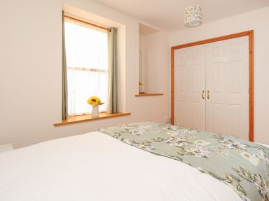 A bedroom with a bed, window with curtains, vase with sunflowers, mirror, and double white closet doors at Bliss On The Bay in Weymouth