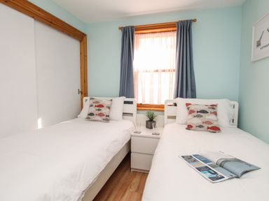 A bedroom with two single beds a small white nightstand with a plant and two glasses and a window with curtains at Bliss On The Bay in Weymouth