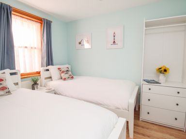A bedroom with two single beds a window with curtains a nightstand a dresser with drawers and framed pictures on the wall at Bliss On The Bay in Weymouth