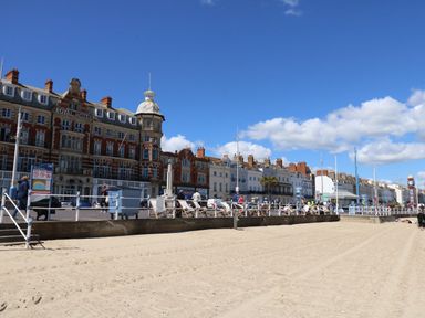 A sandy beach with people sitting on deck chairs and historic buildings in the background at Bliss On The Bay in Weymouth