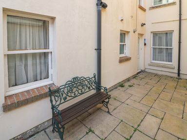 An outdoor patio area with a metal and wooden bench near windows and a door at Bliss On The Bay in Weymouth