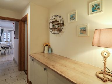 A hallway with a wooden countertop cabinet a lamp framed pictures on the wall and a dining table with chairs in the background at Bliss On The Bay in Weymouth