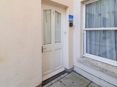 An exterior view of a white door next to a window with sheer curtains at Bliss On The Bay in Weymouth