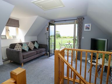 A sitting area with a sofa and cushions a small table with plant a television and doors opening to a patio at Spinney's Den in Knapton