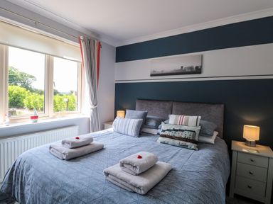 A bedroom with a bed covered in blue bedding and towels placed on top next to a window with curtains at Spinneys Den in Knapton