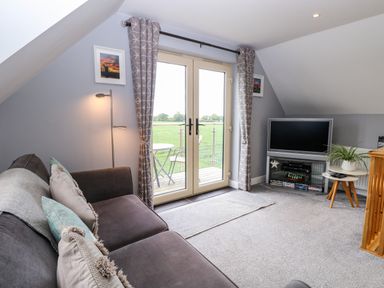 A living room with sofa lamp television and double doors leading to a balcony at Spinney's Den in Knapton