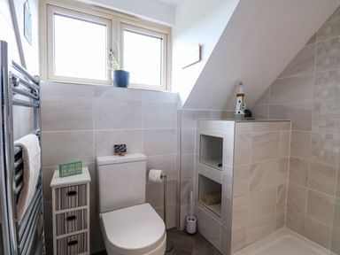 A bathroom with a toilet small cabinet and a tiled shower area at Spinneys Den in Knapton