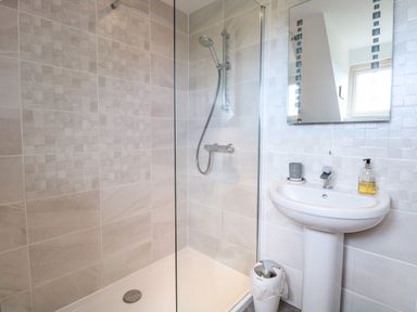 A bathroom with a walk-in shower, a pedestal sink with soap dispenser and candle, a trash bin, and a mirror at Spinney's Den in Knapton