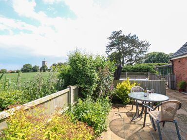 A garden patio with a round glass table and two chairs with wine glasses and a bottle on the table at Spinney's Den in Knapton