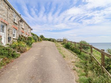 A pathway beside a stone house leading to the ocean at 2 Cliff Cottages West Portholland near Gorran Haven