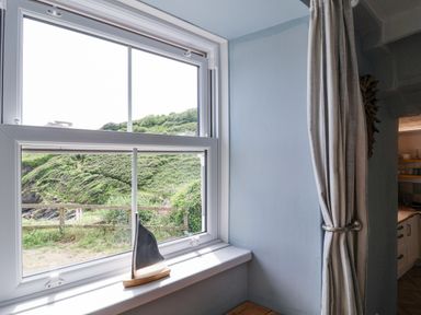 A window with a countryside view and a decorative sailboat at 2 Cliff Cottages West Portholland near Gorran Haven