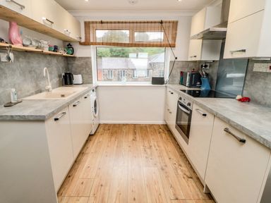 A kitchen with white cabinets gray countertops wooden floor and a window with bamboo blind at Sea Snug in Spittal
