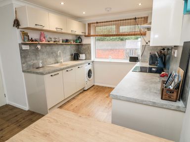 A kitchen with cabinets a washing machine a sink and window with blinds at Sea Snug in Spittal