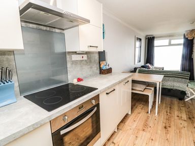 A kitchen with an oven stove countertop and dining table next to a living area with a sofa and window at Sea Snug in Spittal