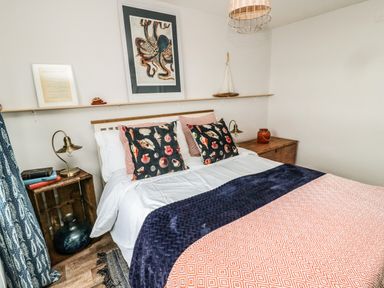 A bedroom with a double bed, decorative pillows, bedside tables with lamps and books, and an octopus artwork on the wall at Sea Snug in Spittal