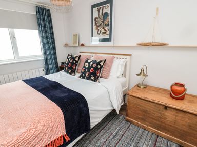 A bedroom with a bed with patterned pillows and a wooden chest with a lamp and vase at Sea Snug in Spittal