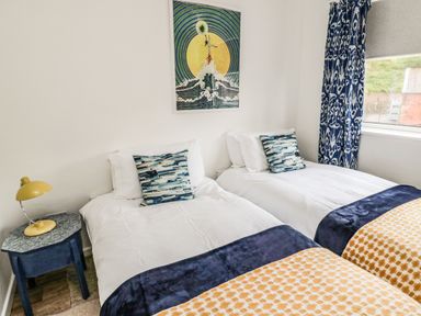 A bedroom with two single beds blue and white pillows and a blue side table with a yellow lamp at Sea Snug in Spittal