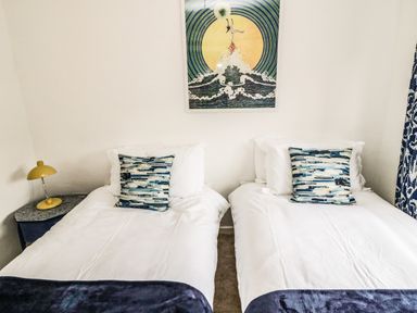 A bedroom with two single beds with white bedding and patterned pillows a yellow lamp on a bedside table and artwork on the wall at Sea Snug in Spittal