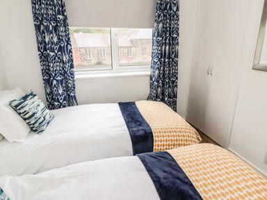 A bedroom with two single beds and patterned curtains at Sea Snug in Spittal