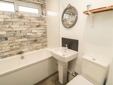 A bathroom with a bathtub a sink a toilet a round mirror and a wooden shelf at Sea Snug in Spittal