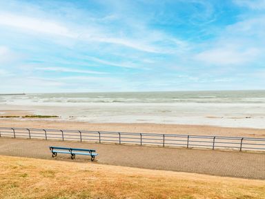 A beach with a bench on a paved walkway next to a grassy area at Sea Snug in Spittal