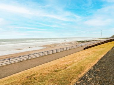 A paved walkway with railings beside a sandy beach and the ocean at Sea Snug in Spittal