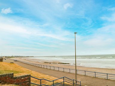 A paved walkway along a sandy beach with railings and a lamppost at Sea Snug in Spittal