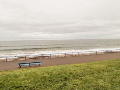 A bench near a walkway with a railing facing the sea and a grassy area in the foreground at Sea Snug in Spittal