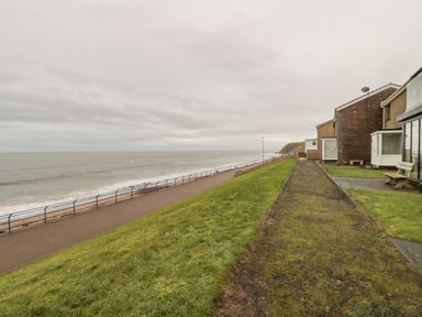 A seaside walkway with railings next to houses and a grassy area at Sea Snug in Spittal