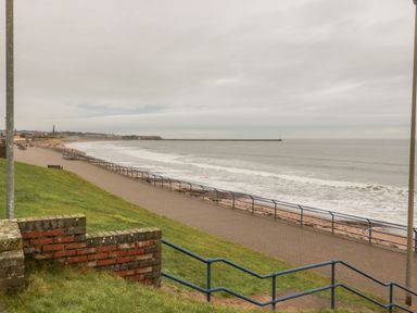 A coastal walkway with railings along a beach and grassy area at Sea Snug in Spittal