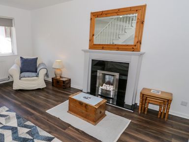 A living room with an armchair a lamp wooden tables fireplace and a mirror at 22 Gwel Yr Wyddfa in Menai Bridge