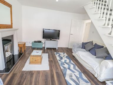 A living room with a sofa under stairs a television on a stand and a fireplace at 22 Gwel Yr Wyddfa in Menai Bridge