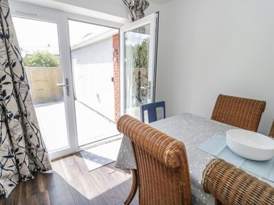 A dining area with wicker chairs around a table covered with a tablecloth and a white bowl near glass doors leading outside at 22 Gwel Yr Wyddfa in Menai Bridge