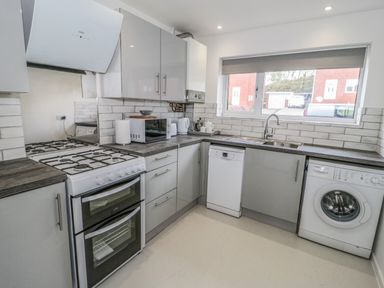 A kitchen with a gas stove dishwasher washing machine microwave and a window at 22 Gwel Yr Wyddfa in Menai Bridge