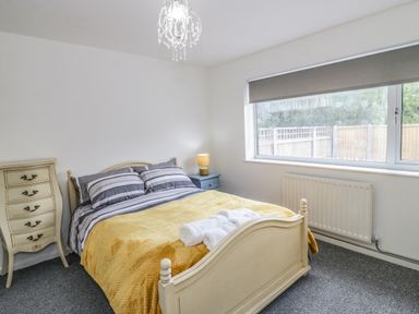 A bedroom with a bed a yellow blanket a bedside table with a lamp and a chest of drawers at 22 Gwel Yr Wyddfa in Menai Bridge