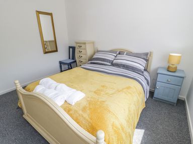 A bedroom with a bed with striped bedding and a yellow blanket with a nightstand and lamp at 22 Gwel Yr Wyddfa in Menai Bridge