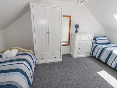 A bedroom with two single beds a white wardrobe a white dresser and a mirror at 22 Gwel Yr Wyddfa in Menai Bridge