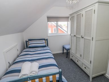 A bedroom with a single bed with striped bedding a wardrobe a stool and a window at 22 Gwel Yr Wyddfa in Menai Bridge