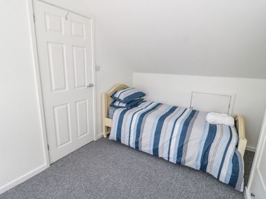 A small bedroom with a single bed with striped blue bedding and a closed white door at 22 Gwel Yr Wyddfa in Menai Bridge