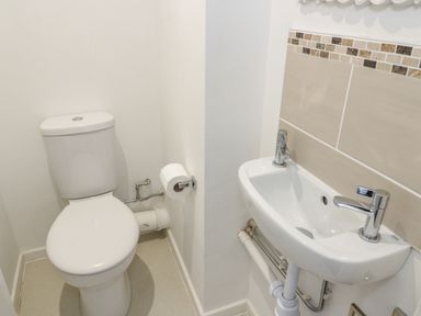 A small bathroom with a toilet and a wall-mounted sink with tiled wall at 22 Gwel Yr Wyddfa Menai Bridge