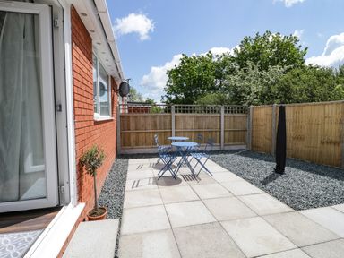 A small outdoor patio with a blue table and four chairs a potted plant and a wooden fence at 22 Gwel Yr Wyddfa in Menai Bridge