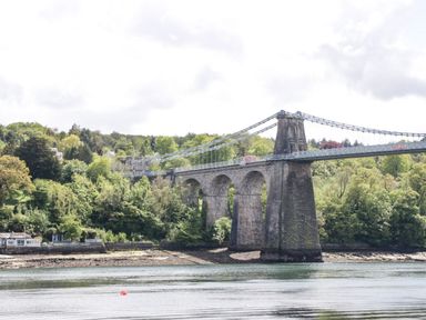 A suspension bridge over a body of water with trees and buildings in the background at 22 Gwel Yr Wyddfa Menai Bridge